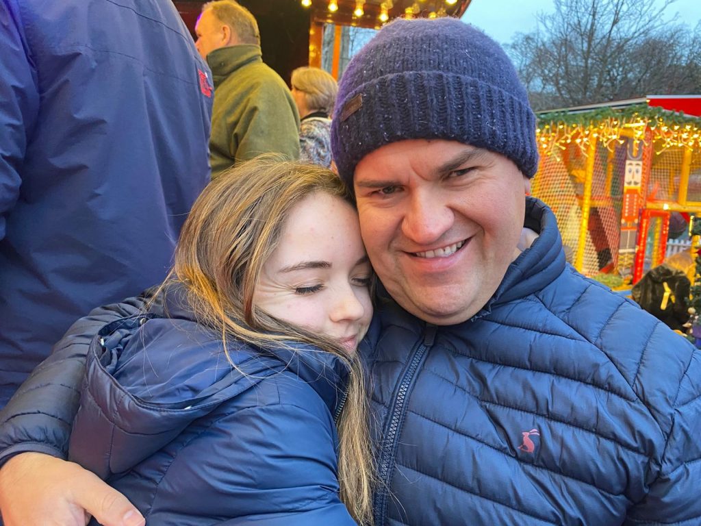 Mark Williams smiling while hugging his daughter at an outdoor event