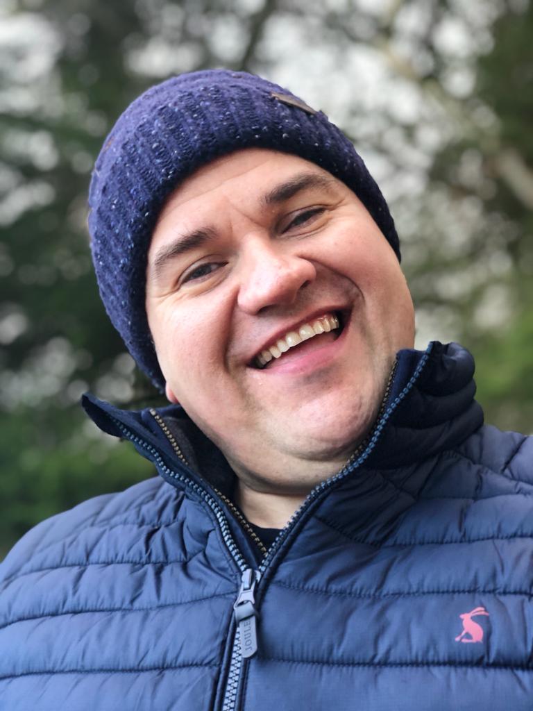 Outdoor portrait of Mark Williams smiling and wearing a navy jacket and beanie